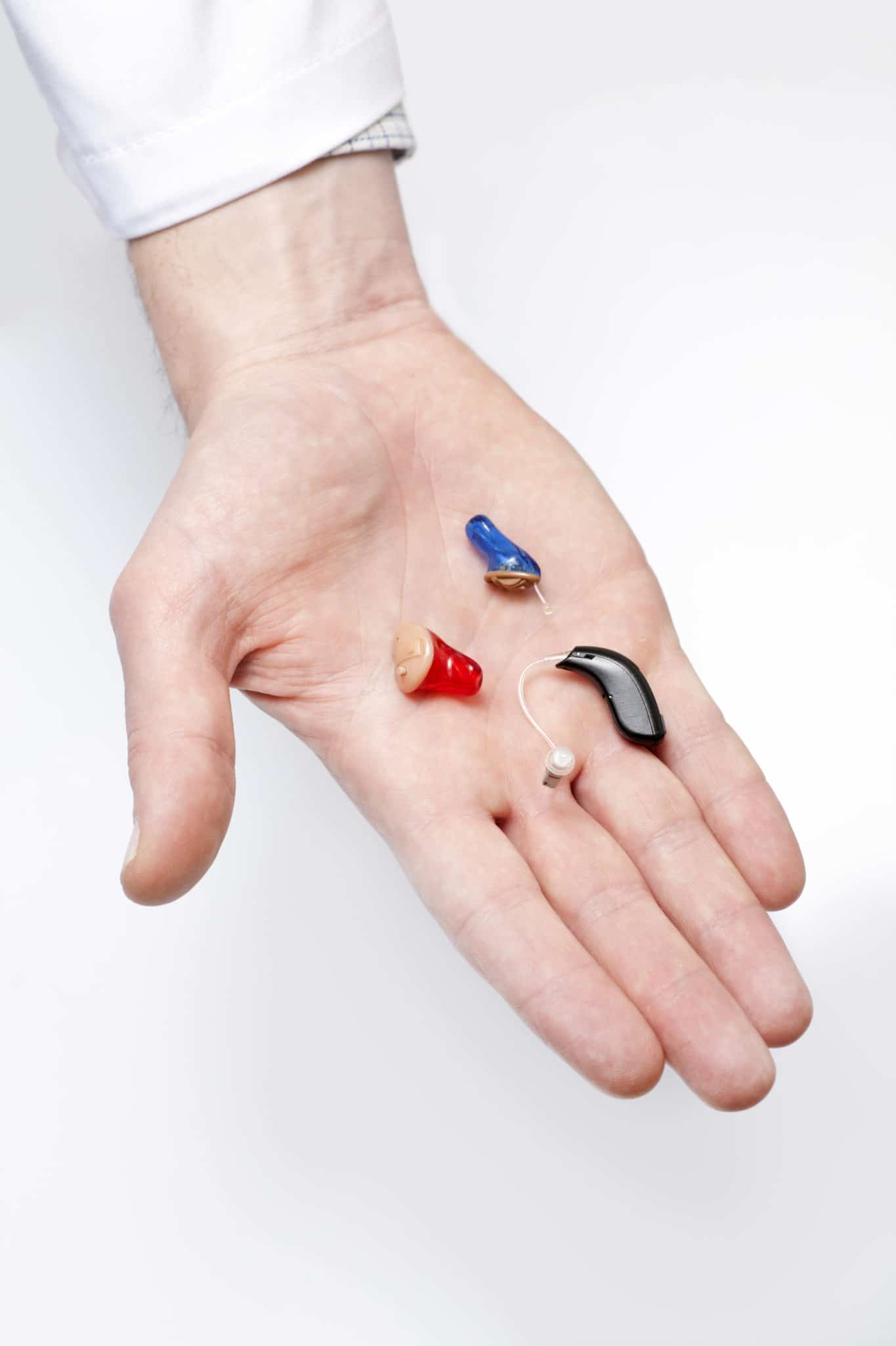 An audiologist's hand holding several hearing aids in Michigan.