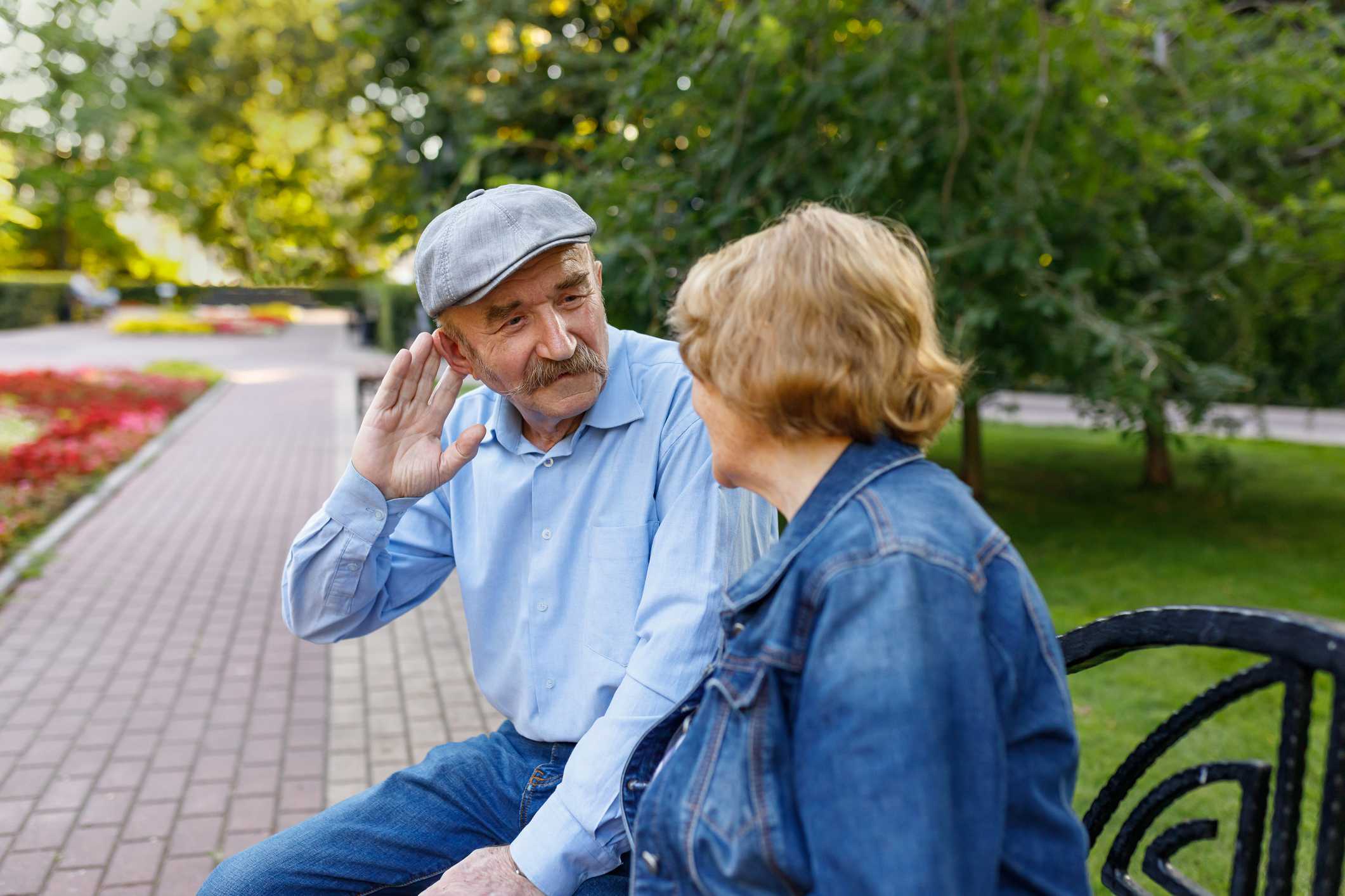 An older Michigan couple sitting in a park but struggling to hear each other because of their hearing loss.